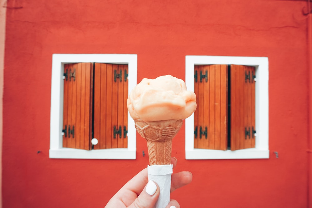 a hand holding an ice cream cone in front of a red building