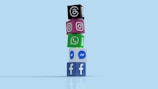 A vertical stack of colorful cubes, each displaying a logo of different social media platforms including Facebook, Messenger, WhatsApp, Instagram, and Threads, placed against a light blue background.