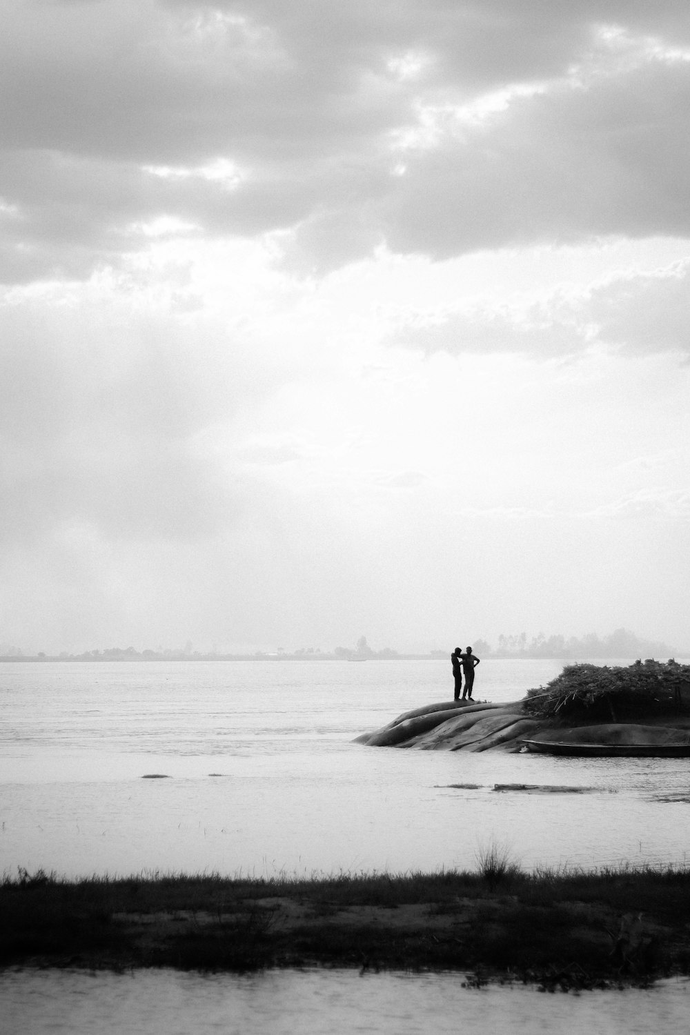 a black and white photo of two people standing on a small island