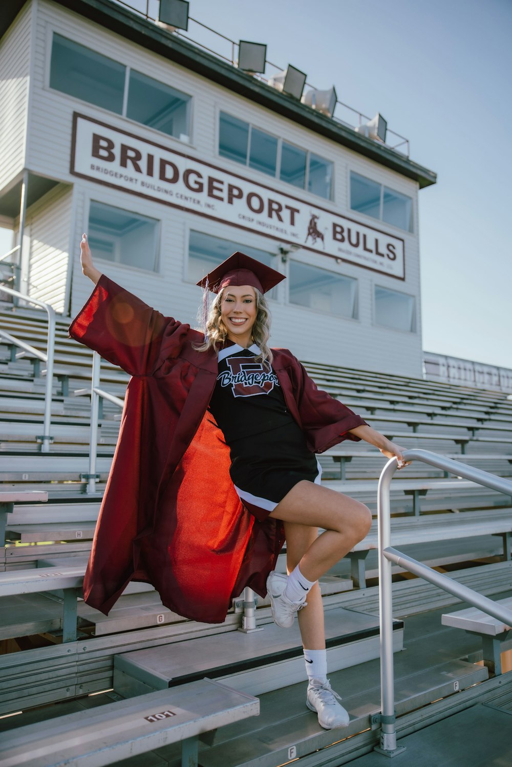 a woman in a graduation cap and gown posing on a bleachers