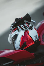 A sleek red motorcycle helmet resting on a polished wooden table beside a laptop and a notepad.
