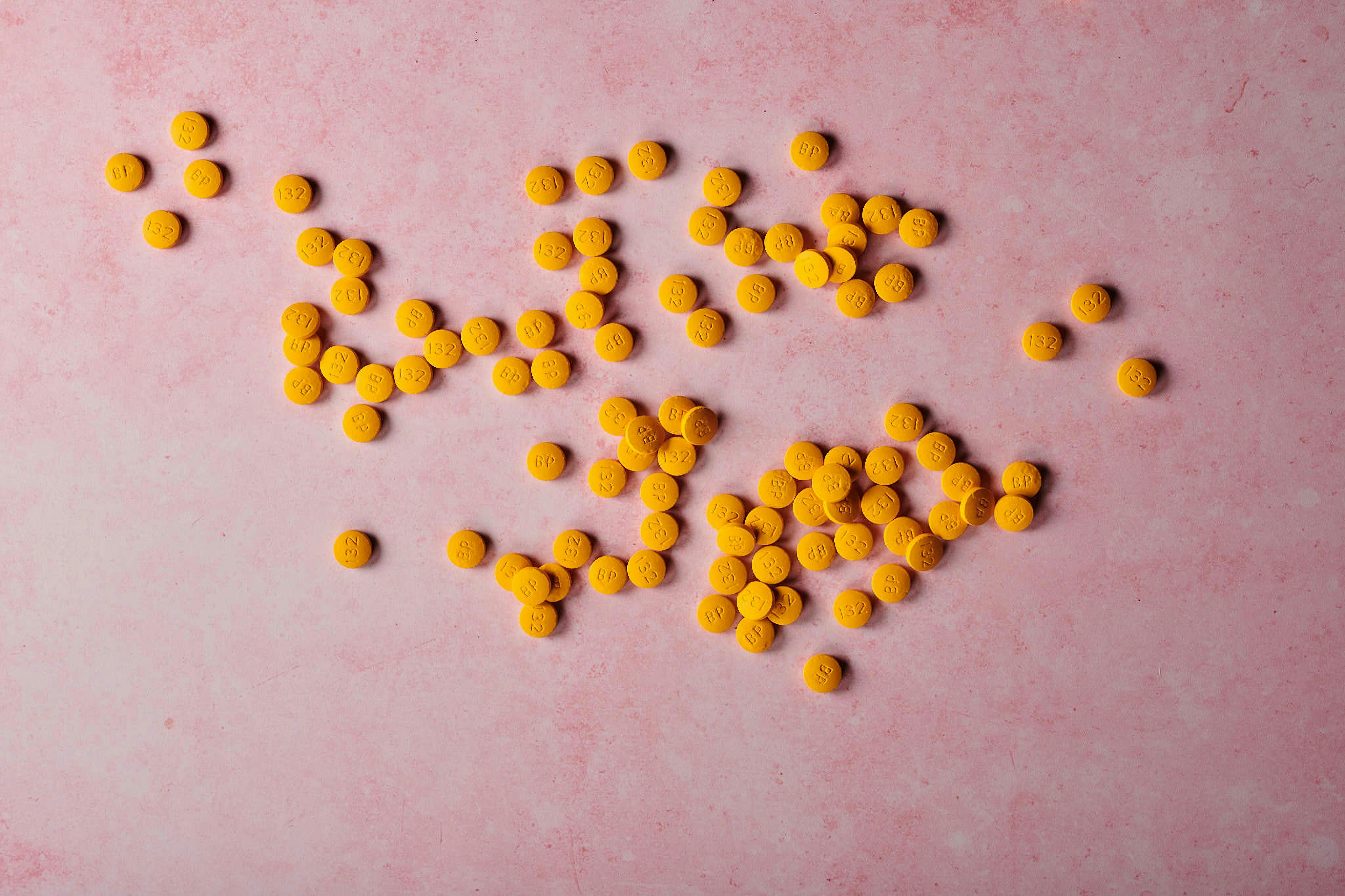 a pile of yellow pills sitting on top of a pink surface