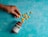 A hand is picking up one of the scattered yellow tablets that have spilled from a brown bottle labeled 'Beelith Tablets'. The bottle lies on a textured teal surface.