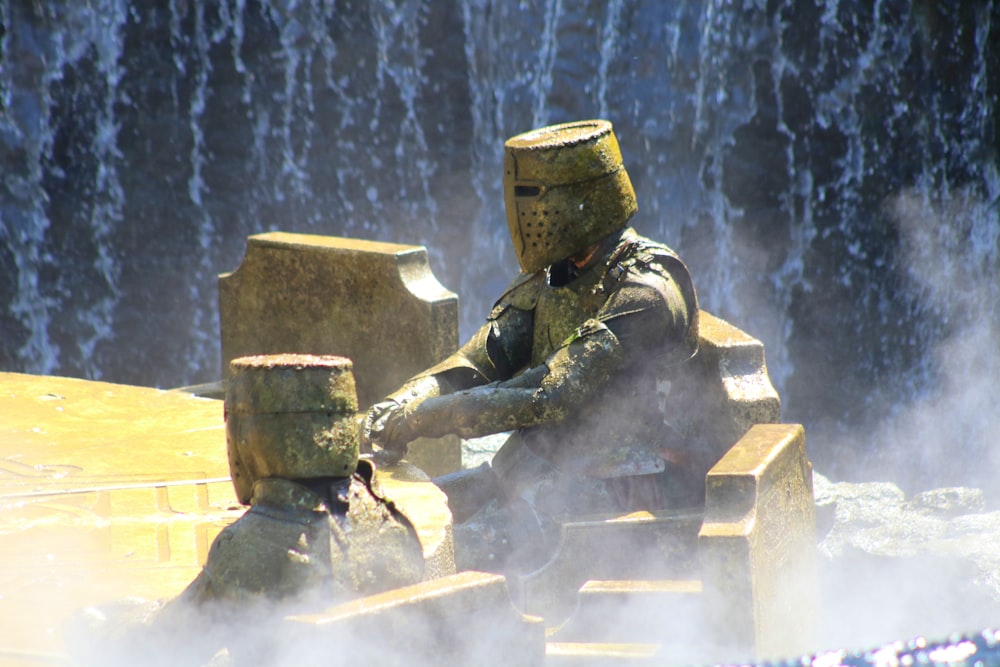 a statue of a man sitting on a bench in front of a waterfall