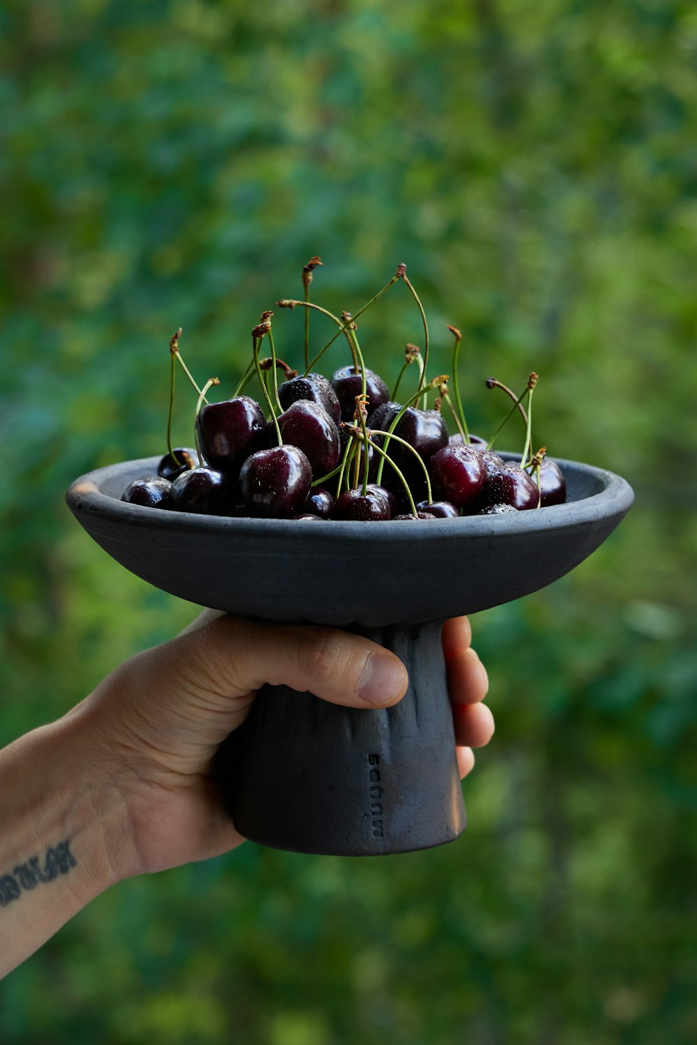a person holding a black bowl filled with cherries