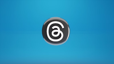 A black circular symbol with an abstract white design resembling a swirling line pattern is placed against a blue gradient background.