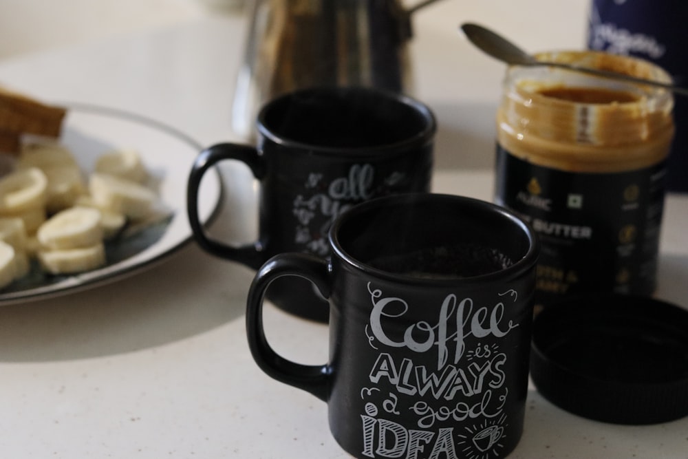 two coffee mugs sitting on a table next to a plate of bananas