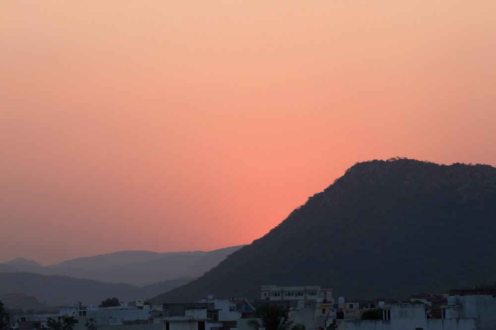 the sun is setting over a city with a mountain in the background