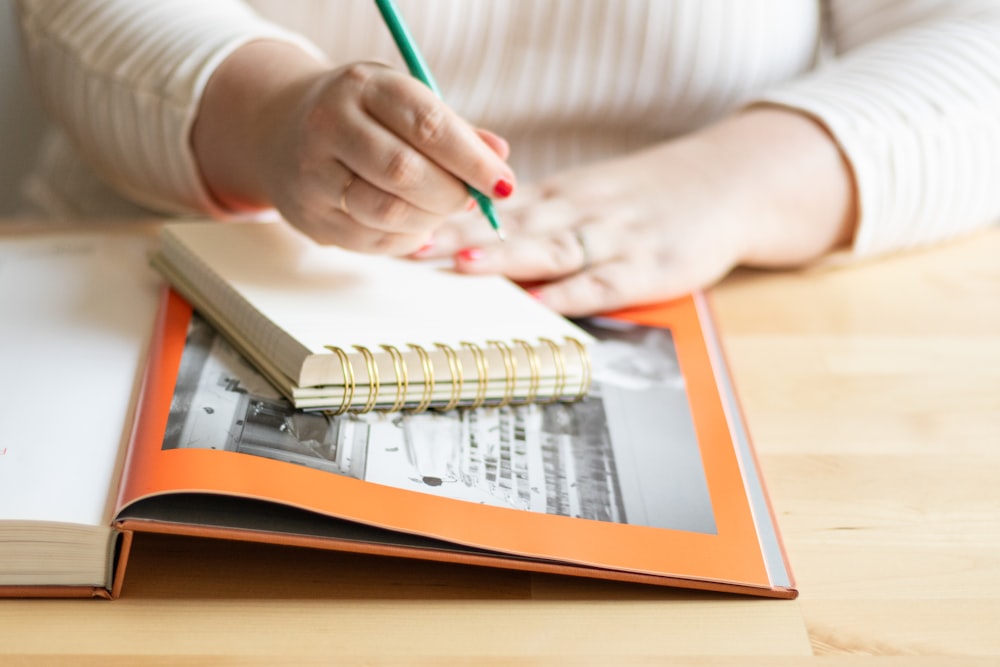 a person writing on a notebook with a pencil