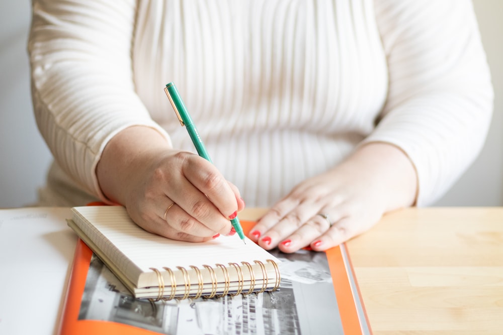 a woman writing on a notebook with a pencil
