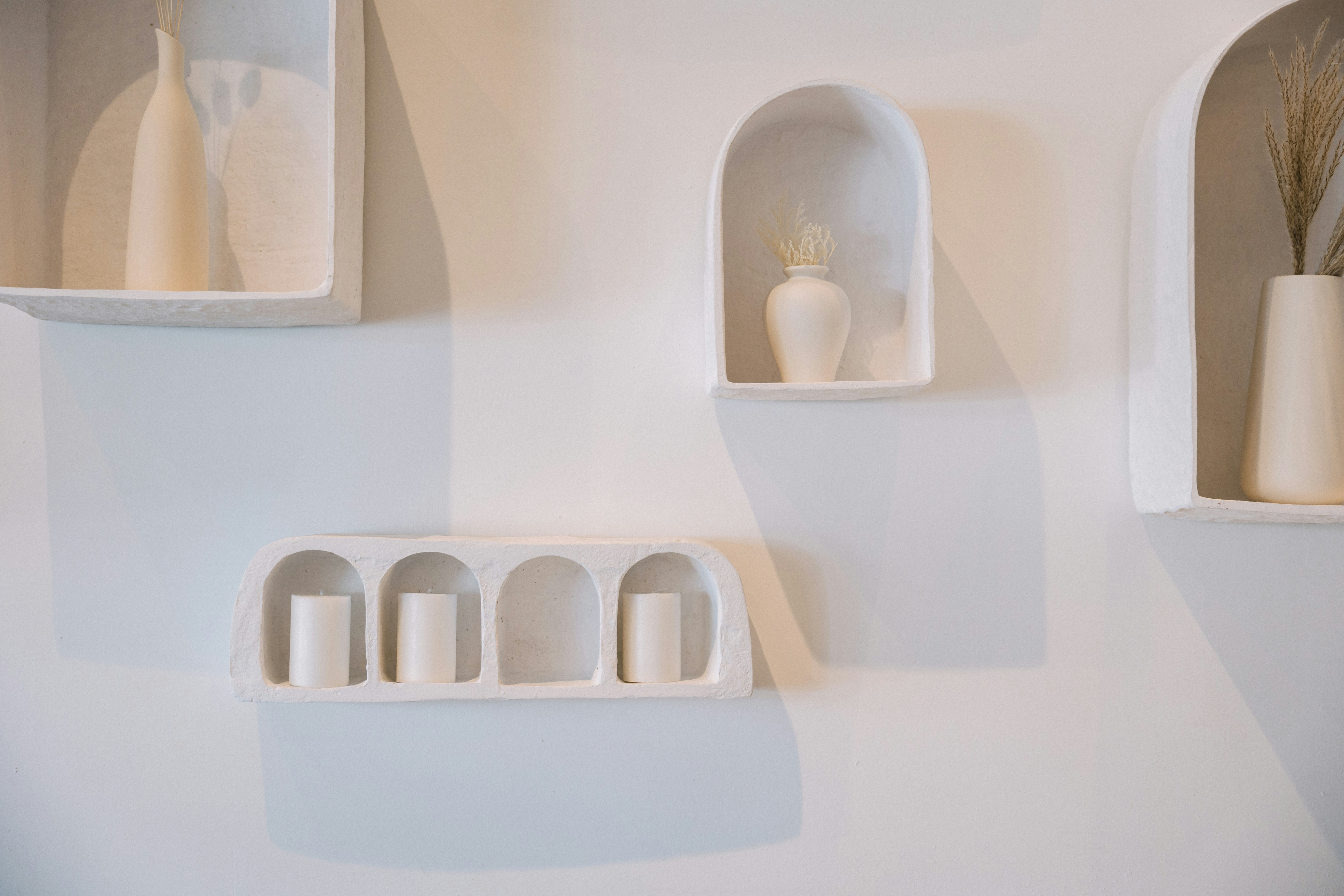 a white wall with three white vases on it