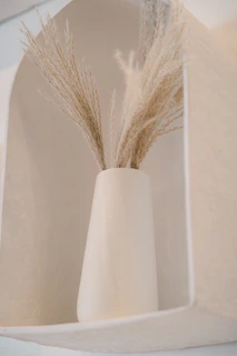 A rustic terracotta vase with subtle texture, holding dried pampas grass on a minimalist side table