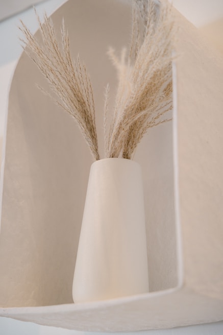 Minimalist arrangement of dried flowers and pampas grass in a clear glass vase on a white surface