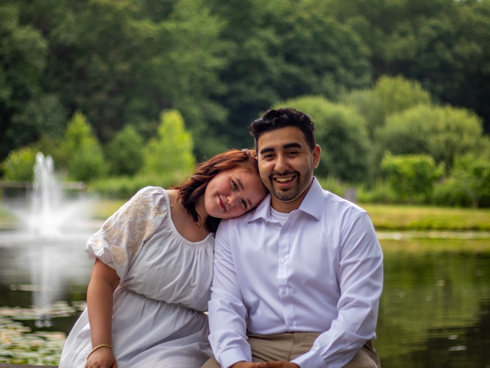 a man and a woman sitting next to each other in front of a pond