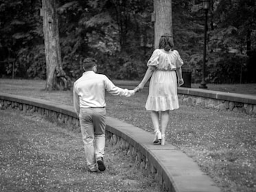 A wide shot of a couple walking hand in hand through a sunlit garden pathway.