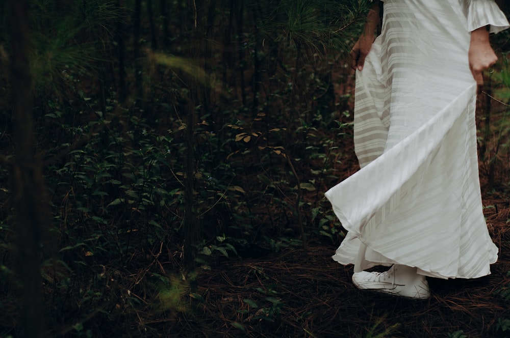 a woman in a white dress walking through a forest