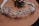 A delicate headband decorated with intricate floral and pearl designs is placed on a wooden surface. The headband features small white flowers, pearls, and metallic elements, giving it an elegant and ornamental appearance.