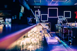 A sleek modern bar counter with bottles illuminated by soft red and white neon lights.