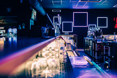 A sleek modern bar counter with bottles illuminated by soft red and white neon lights.