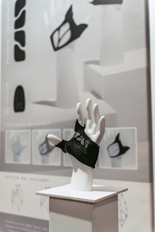 A mannequin hand mounted on a stand is wearing a black glove with intricate designs. The background includes various conceptual sketches and designs, showcasing different perspectives of the glove. The overall style is modern and artistic, with a focus on design and aesthetics.