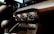 The interior of a car featuring the dashboard and air conditioning controls. The controls include dials for adjusting temperature and fan settings. The dashboard is detailed with black and brown materials, and noticeable orange stitching adds a touch of contrast.