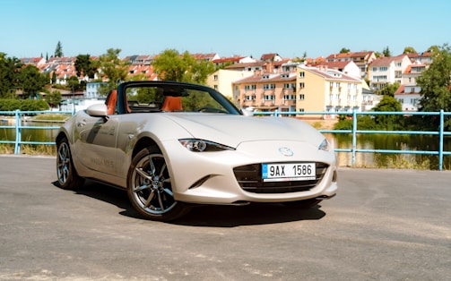 Close-up of a Mazda MX-5 convertible with its top down, parked near a scenic vineyard.