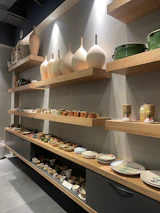 Finished ceramic pieces displayed on wooden shelves, showcasing various styles and glazes.