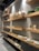 A series of wooden shelves displaying various ceramic items such as vases, mugs, bowls, and plates. Large, elegantly shaped vases stand prominently on the higher shelf, while smaller mugs and dishes occupy the lower shelves. The shelves are lit by overhead lighting, enhancing the earthy tones of the ceramics.