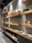 A series of wooden shelves displaying various ceramic items such as vases, mugs, bowls, and plates. Large, elegantly shaped vases stand prominently on the higher shelf, while smaller mugs and dishes occupy the lower shelves. The shelves are lit by overhead lighting, enhancing the earthy tones of the ceramics.