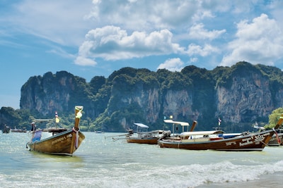 A traditional longtail boat gliding through turquoise waters near a limestone cliff.