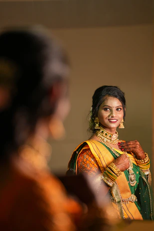 A smiling woman admiring her reflection while wearing a beautifully detailed saree.
