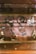 A display case containing jewelry pieces including necklaces and rings. The items have price tags such as $90, $295, and $475, indicating value. The jewelry pieces are arranged neatly on a reflective surface, enhancing their metallic sheen.