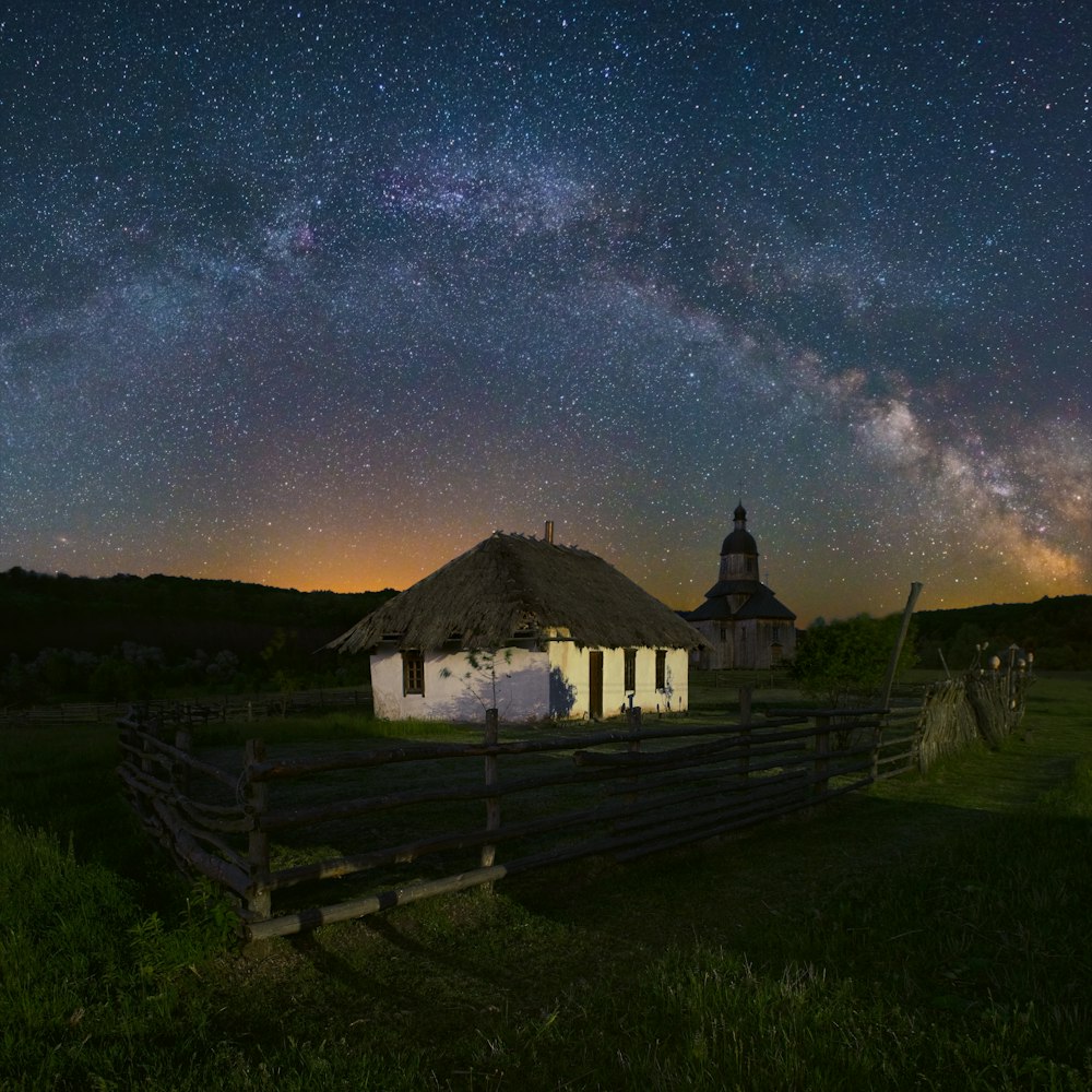 a barn with a thatched roof and a night sky filled with stars