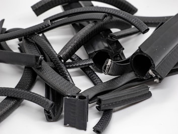 A collection of various black, cylindrical and rectangular rubber pieces with textured surfaces, some of which are partially open revealing metallic clips or inner components, arranged randomly on a flat, light-colored surface.