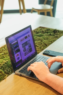 A focused designer working on a laptop with dark forest green accents visible on the screen.