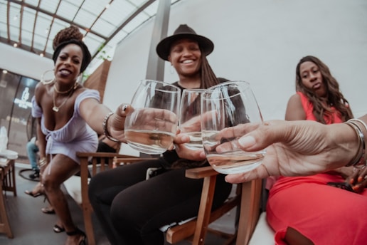 A group of people are gathered in a social setting, holding glasses filled with a light-colored drink. They appear to be toasting or celebrating. The atmosphere seems relaxed and joyful, with a mix of casual and dressy attire.