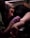 A tattoo artist is carefully working on a design on a person's arm in a dimly lit environment. The artist is wearing a pink glove, attentively focused on the task. The person receiving the tattoo is lying down with their arm positioned on a cushioned rest. The scene conveys concentration and precision.