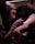 A tattoo artist is carefully working on a design on a person's arm in a dimly lit environment. The artist is wearing a pink glove, attentively focused on the task. The person receiving the tattoo is lying down with their arm positioned on a cushioned rest. The scene conveys concentration and precision.