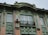 A detailed facade of a building featuring ornate architectural elements. The design includes intricate carvings and sculptures framing the windows, with an air conditioning unit mounted on one side. The structure is primarily adorned in a mint green color with contrasting beige brickwork.