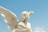 A stone sculpture of an angel with long flowing hair and large wings, set against a clear blue sky.