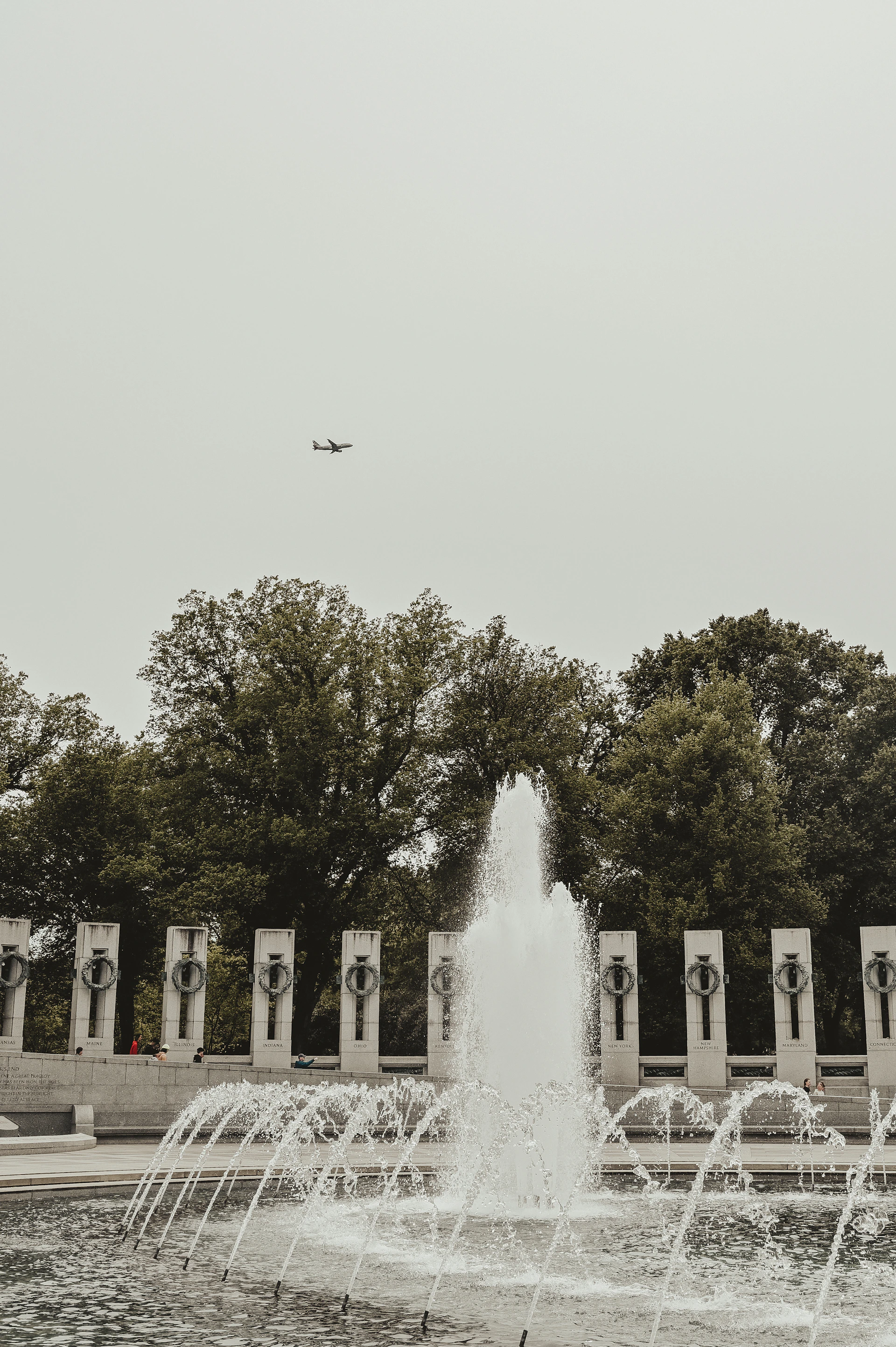 a jet flying over a fountain in a park