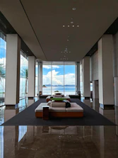 A minimalist, sunlit hotel lobby with elegant white furnishings and ocean views.