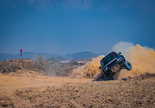Dust swirling behind a speeding Baja race truck crossing rugged desert terrain.