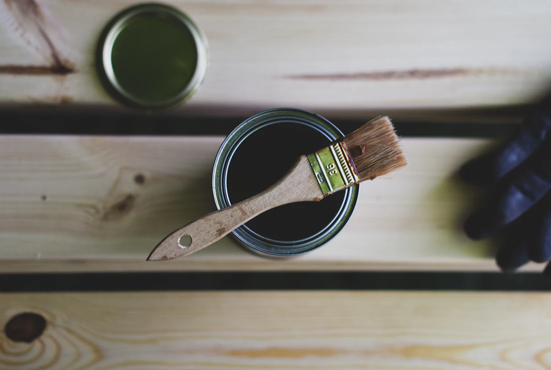 Open can of wood stain with a brush resting on a board