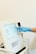 A hand wearing a blue glove is interacting with a touchscreen monitor. The device appears to be part of medical or laboratory equipment. The interface displays various settings and options.