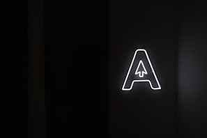 A large, glowing letter 'A' with a stylized arrow pointing upwards inside it is placed against a dark background, emitting bright white light.