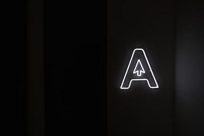 A large, glowing letter 'A' with a stylized arrow pointing upwards inside it is placed against a dark background, emitting bright white light.
