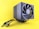 A computer cooling fan or air cooler with a large, black circular fan is connected with multiple cables and placed against a bright yellow background. The design is sleek and modern, featuring a metallic grid structure.