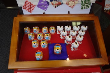 A display case contains a collection of small animal figurines. The figures are intricately painted and include a variety of styles. The background features decorative, colorful paper patterns.