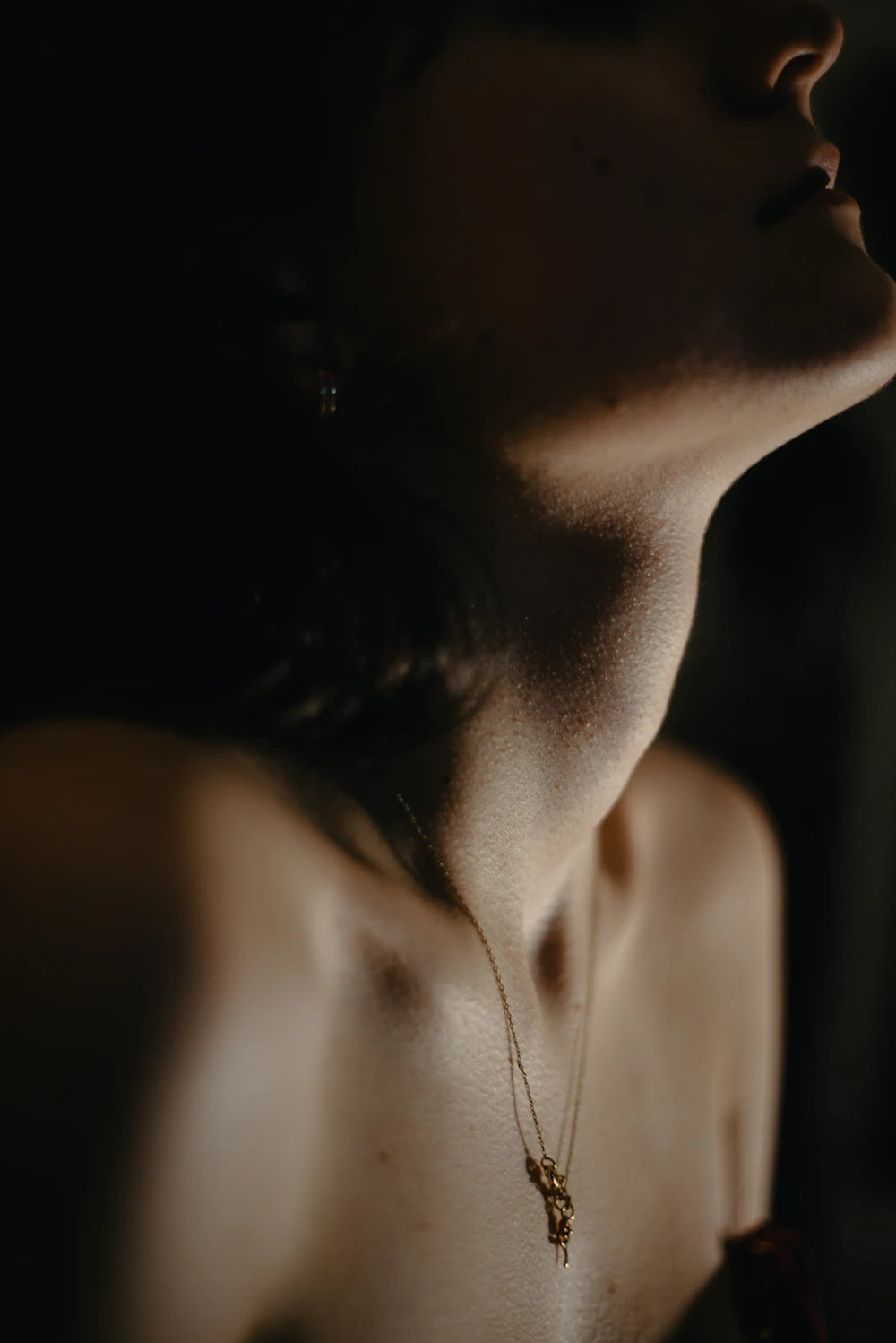 Intimate editorial detail of a collarbone and a fine necklace in warm low light.
